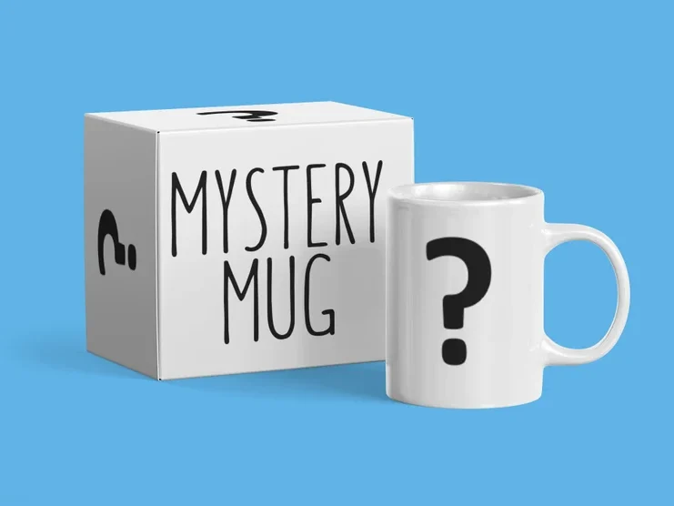 Father’s Day Gifts For a Dad Who Has Everything - Light blue background with a white coffee mug that has a black question mark on it. With a box that says Mystery mug. 