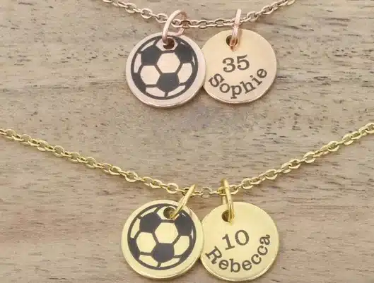Rose and gold necklaces, both with round charms with a childs name and number on it, and another round one with a soccer ball on it. 