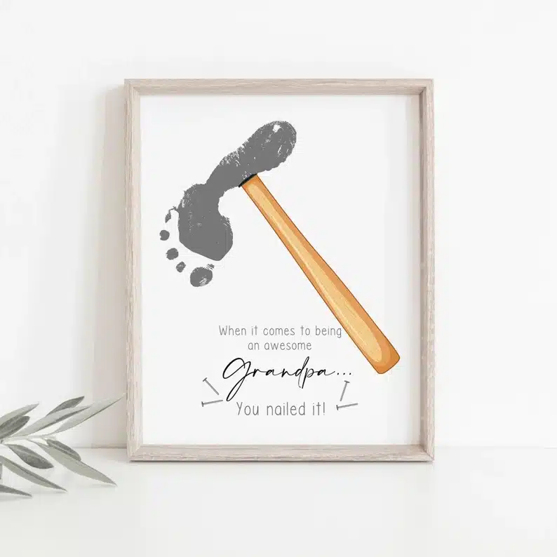 Framed white print of a grey footprint made to look like a hammer. Font below says "when it comes to being an awesome Grandpa you nailed it!" 