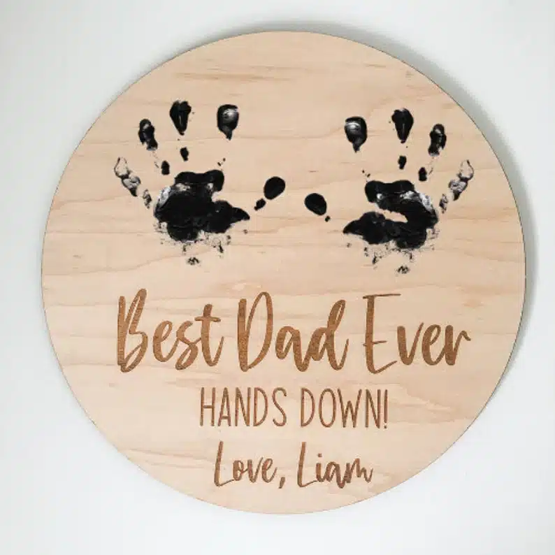 Round wooden sign with two handprints on it that says Best dad ever hands down love, Liam. 