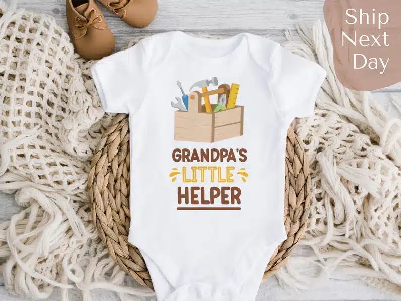 White baby onesie with a tool box on it that says Grandpa's little helper below. 