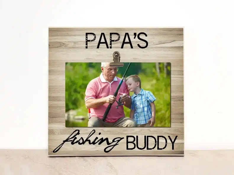 Wooden frame with black font that says Papa's fishing buddy. 
