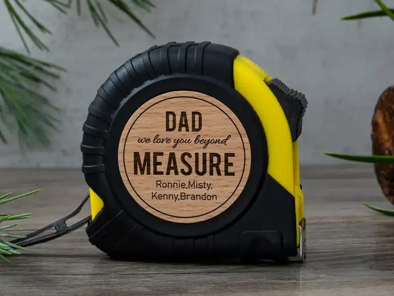 Father’s Day Gifts For Hard to Buy For Dads - black and yellow tape measurer with a round wooden style middle that says Dad we love you beyond measure. 