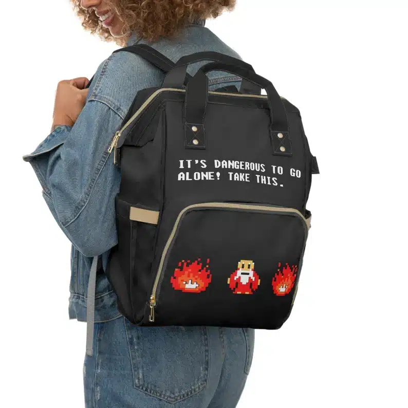 Black diaper backpack that says It's dangerous to go alone! Take this! and characters from Zelda game. 