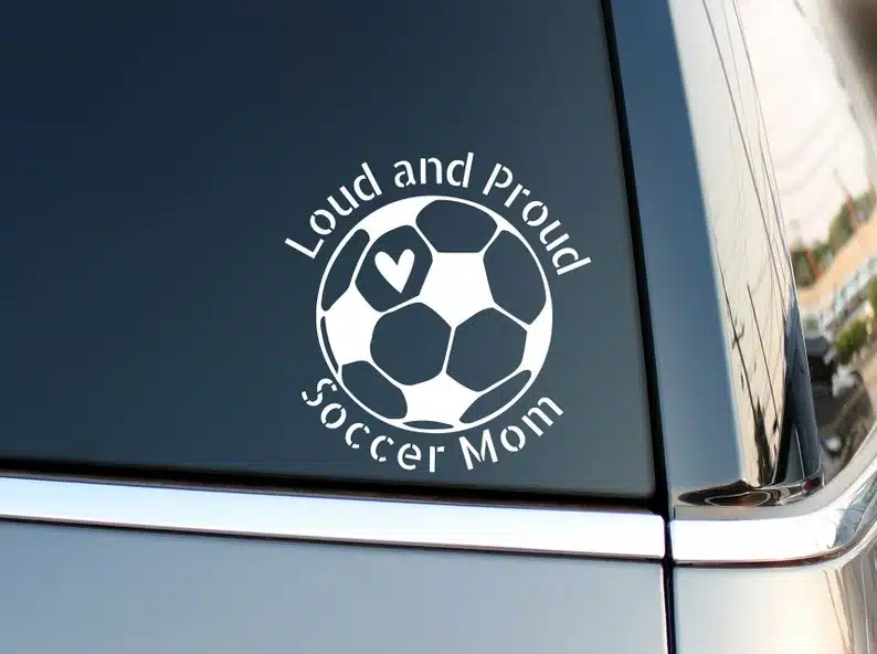 Back of a car window with a white vinyl sticker on it that says Loud and proud soccer mom with a soccer ball. 