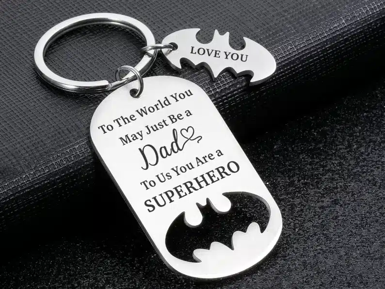 Custom keychain with a batman symbol charm, and a larger charm that says To the world you may just be a dad to us you are a superhero. 