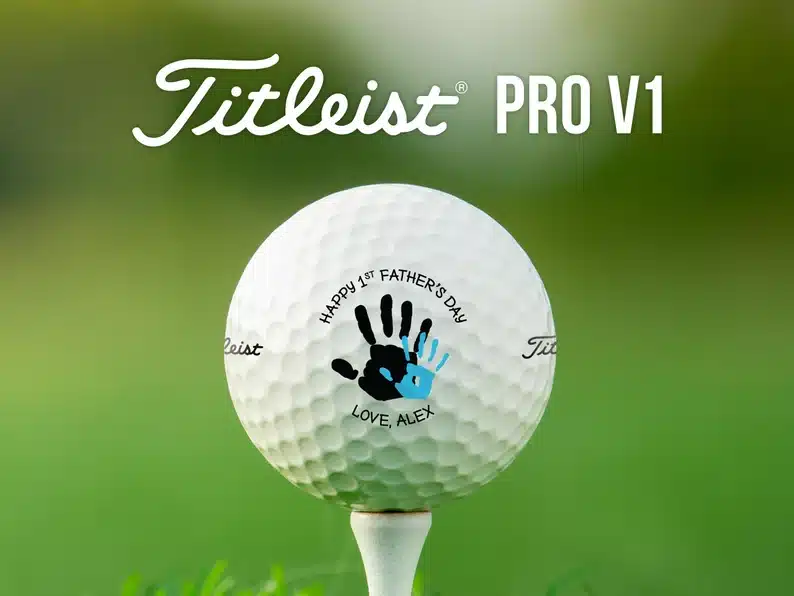 Father's Day golf ball, white golf ball with a larger black handprint and a smaller blue handprint that says Happy 1st Father's Day Love Alex. 