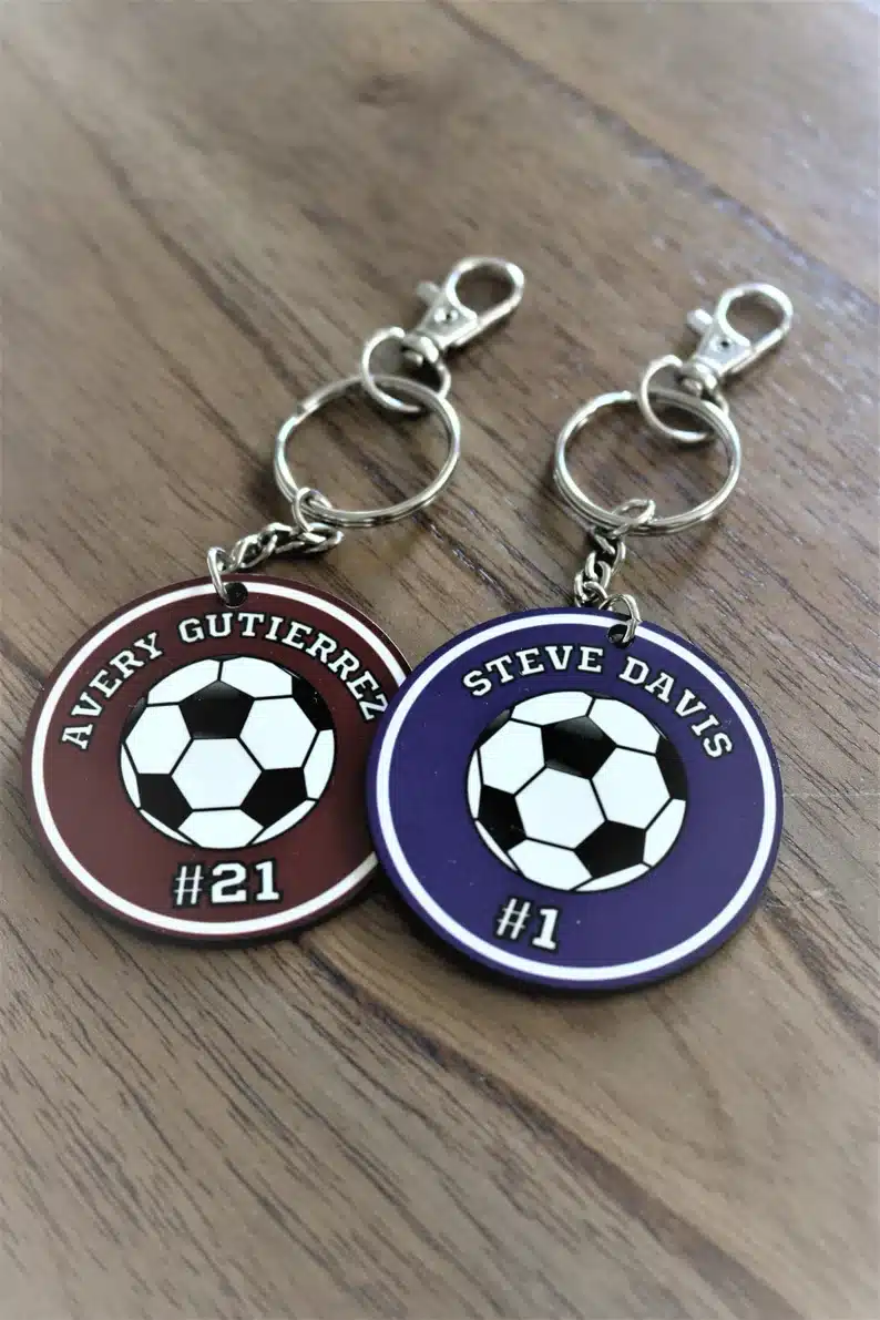 Two silver soccer ball name tags, one burgundy and one blue. 