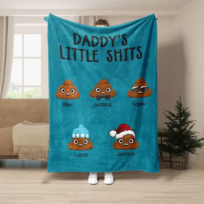 Blue blanket with five cartoon pops on it, each with a differnt kids name below it. Above Daddy's little shits in black ink