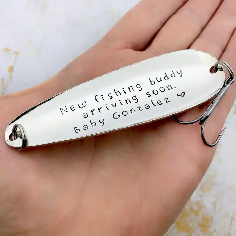 Silver fishing hook that says "New fishing buddy arriving soon. Baby Gonzalez" 