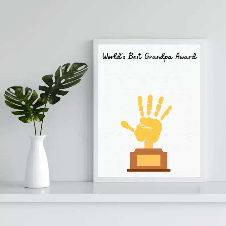White print with a golden handprint made to look like a trophy with black font above that says "World's Best Grandpa Award" 