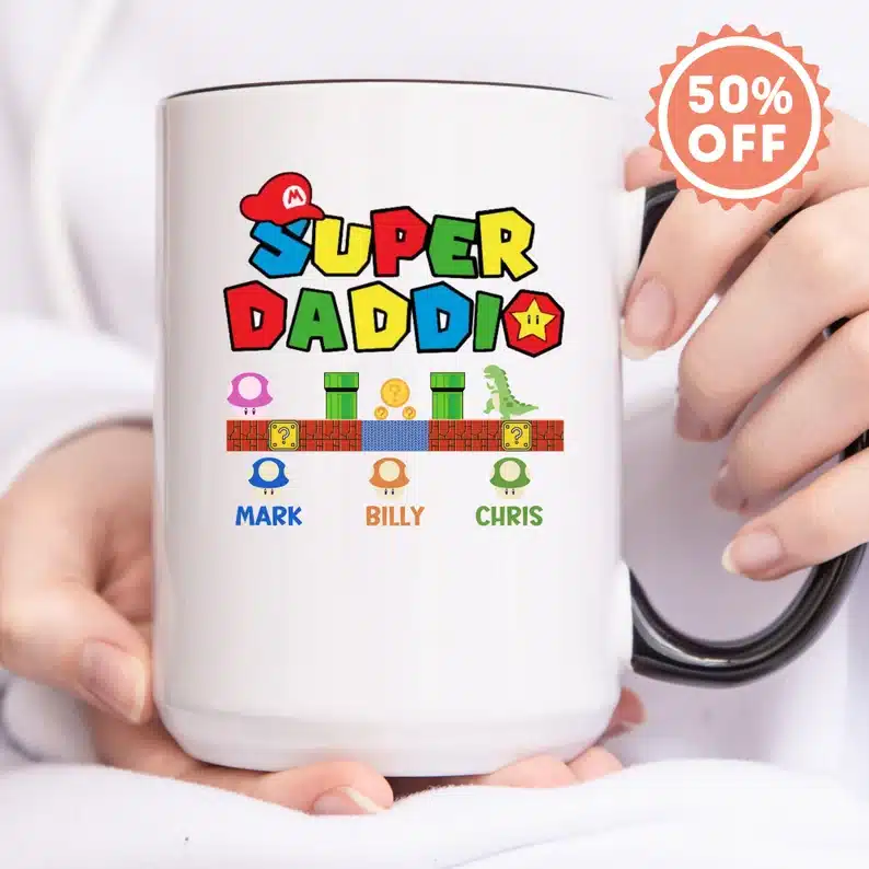 Close up of hands holding a white coffee mug with super Mario themed photos and font that says "Super Daddio" 