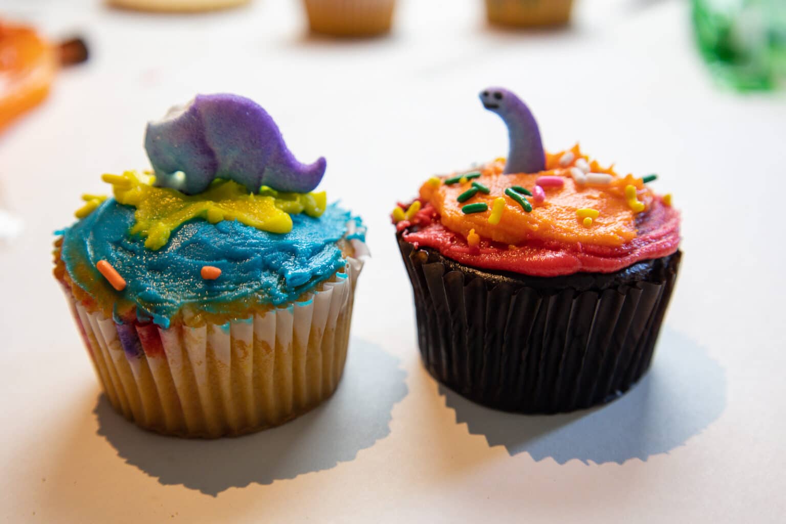 Two cupcakes with a broken dinosaur on top