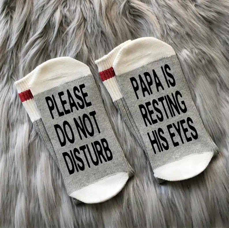 Father’s Day Gifts For Papa - Grey and white socks that say Please do not disturb on one sock and papa is resting his eyes on the other sock in black print.