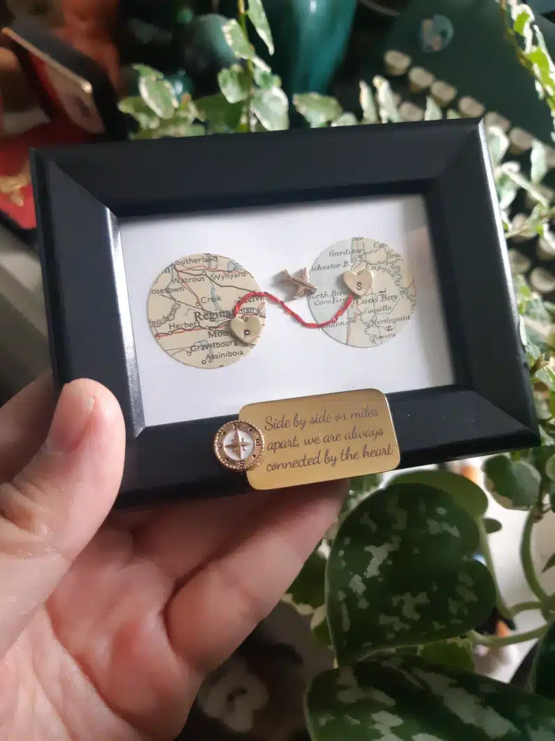 Mini black framed white print showing two circles of two differnt locations and a tiny gold plane. 