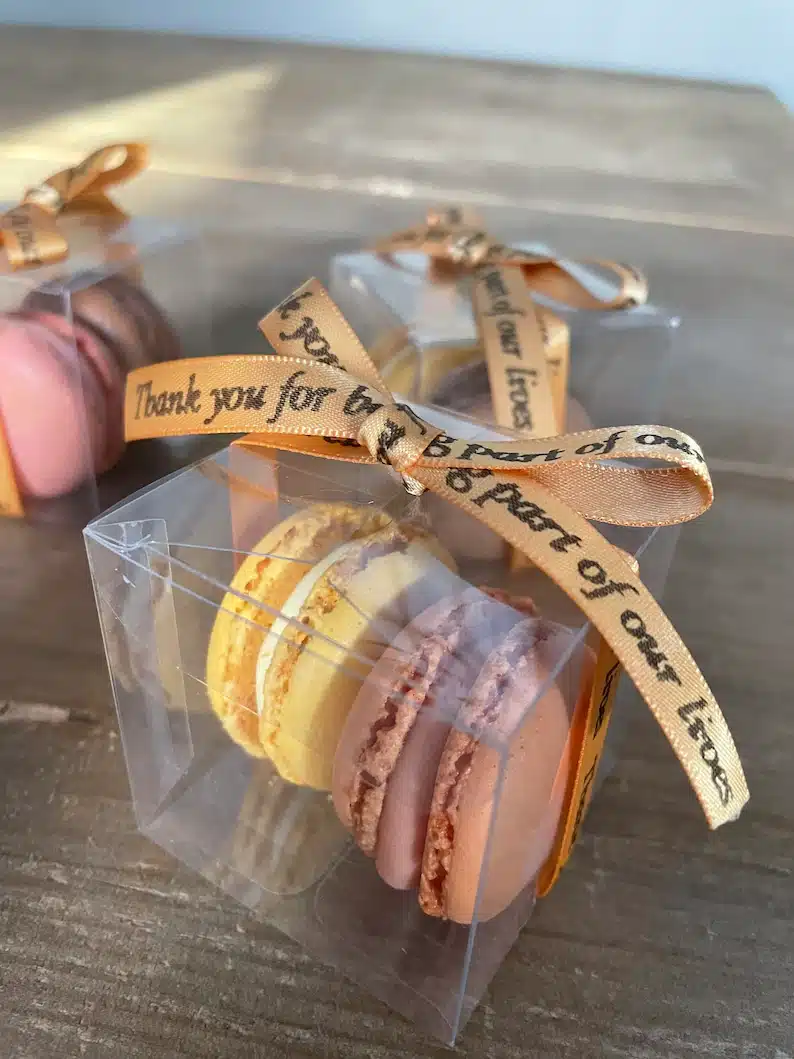CLear box with two macarons in it, one yellow and one light brown. 