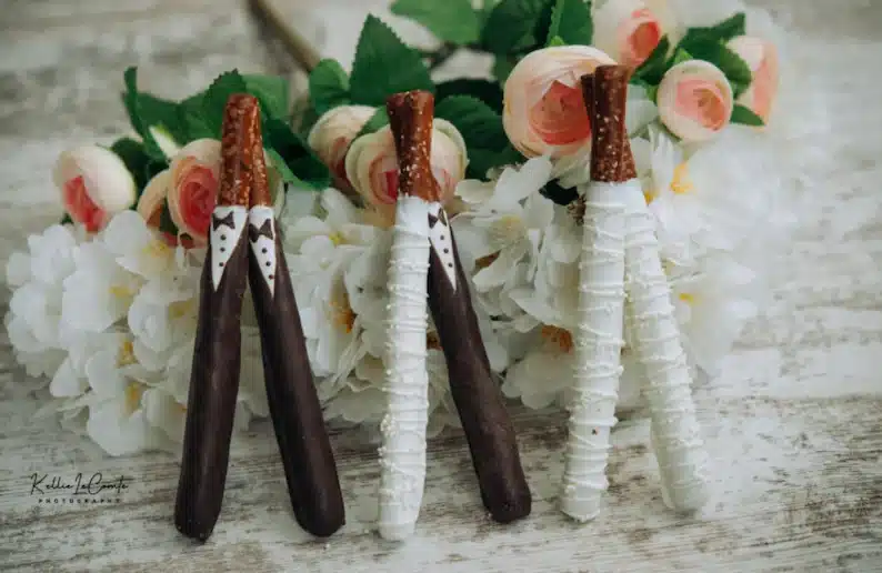 Pretzel rods dipped in white and chocolate made to look like a bride and groom. 