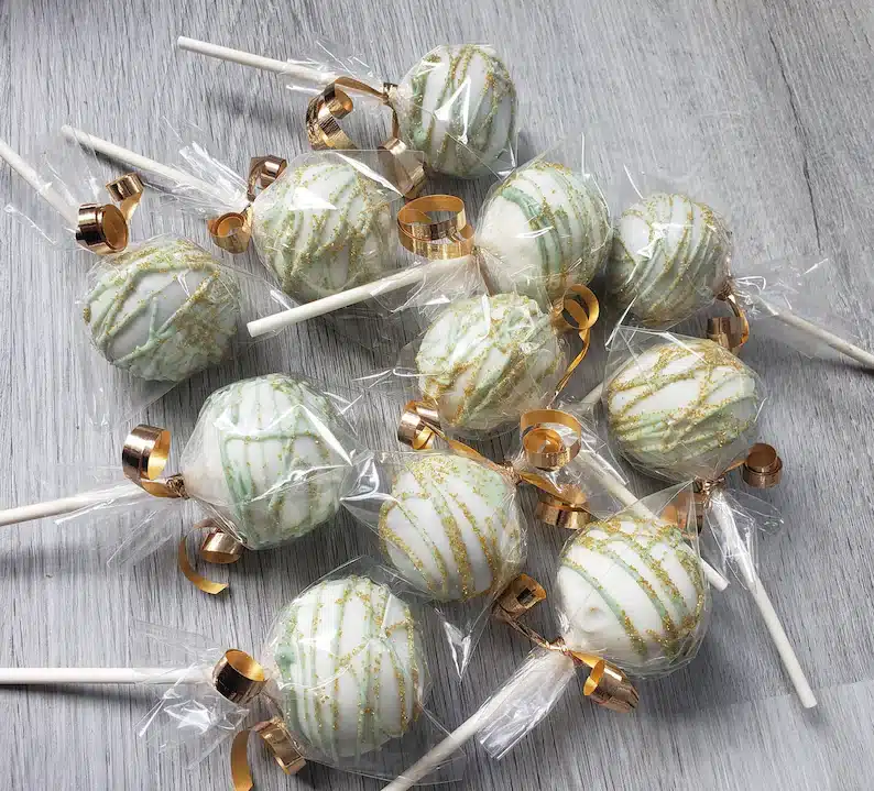 Various white and gold cake pops all wrapped in clear wrapper with gold string. 