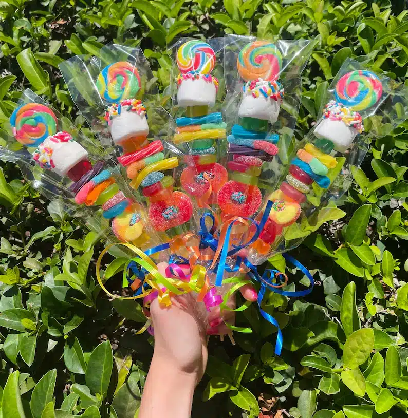 The Most Delicious Edible Wedding Favors - hand holding various candy kabobs each with different gummies and marshmallows on it. 