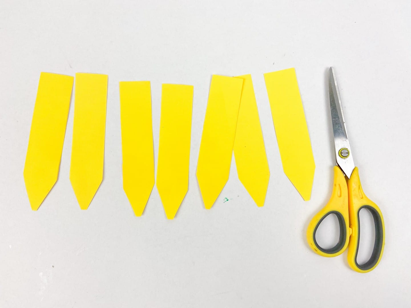 Yellow scissors beside yellow cut outs shaped like pencils. 