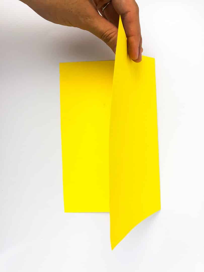 A hand folding a piece of yellow paper in half. 