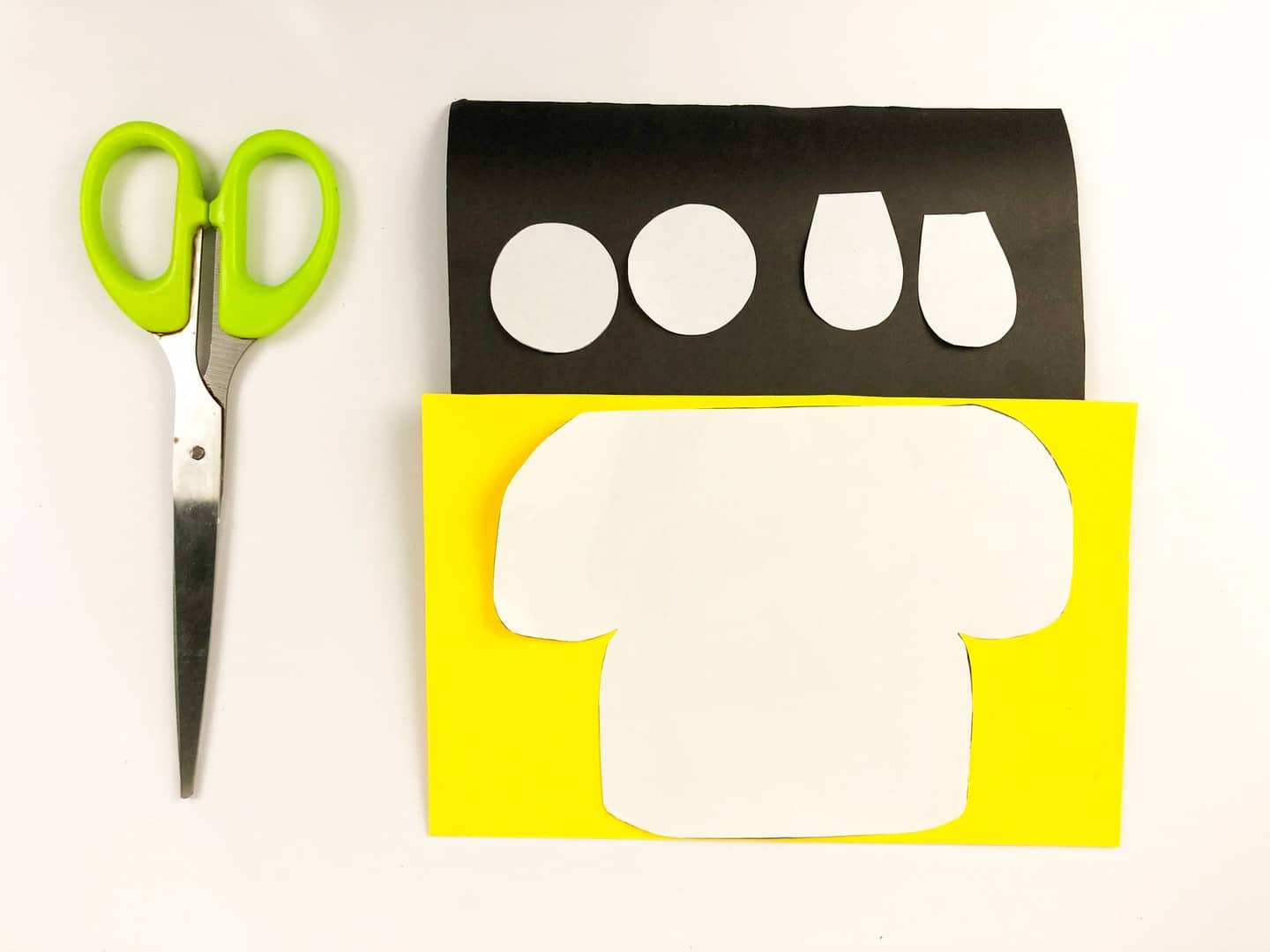 Scissors beside yellow paper with white paper tracer on it and black paper with white tracers of circles on it. 