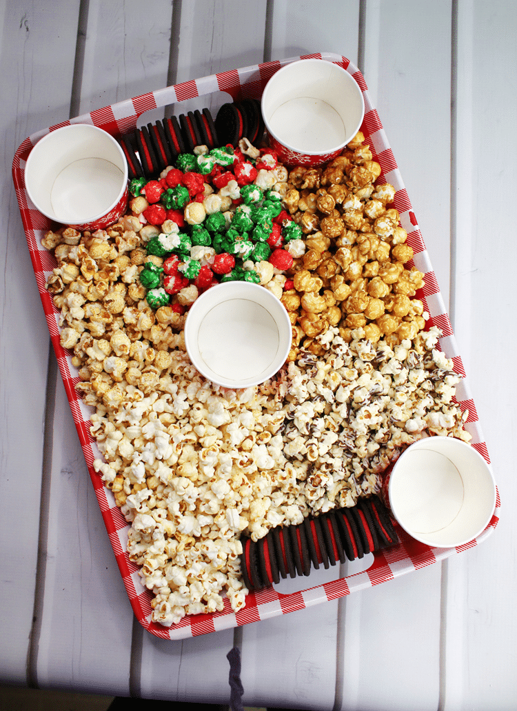 Above view of holiday board with festive cups still emptied but popcorn and cookies filled around it.