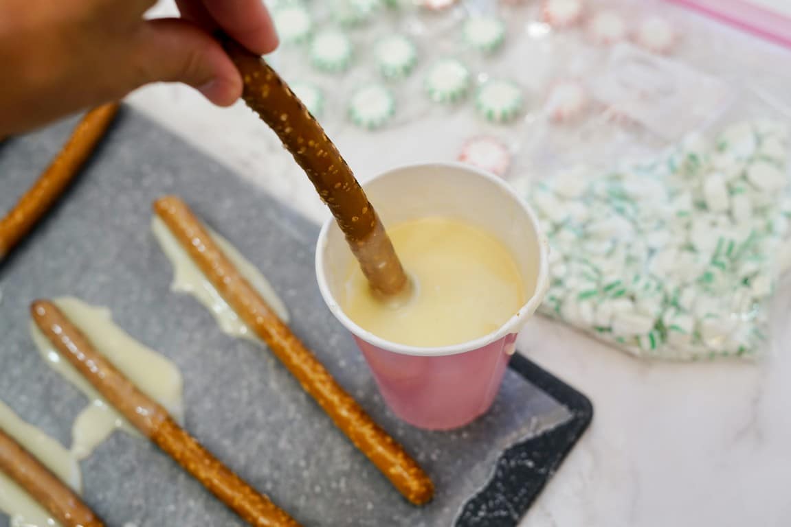 Paper cup with melted white chocolate in it and a pretzel being dipped into it.