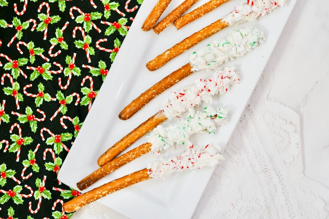 Christmas White Chocolate Peppermint Pretzel Rods - white rectangle plate with pretzels rods on them each dipped in white chocolate and rolled in peppermint pieces.