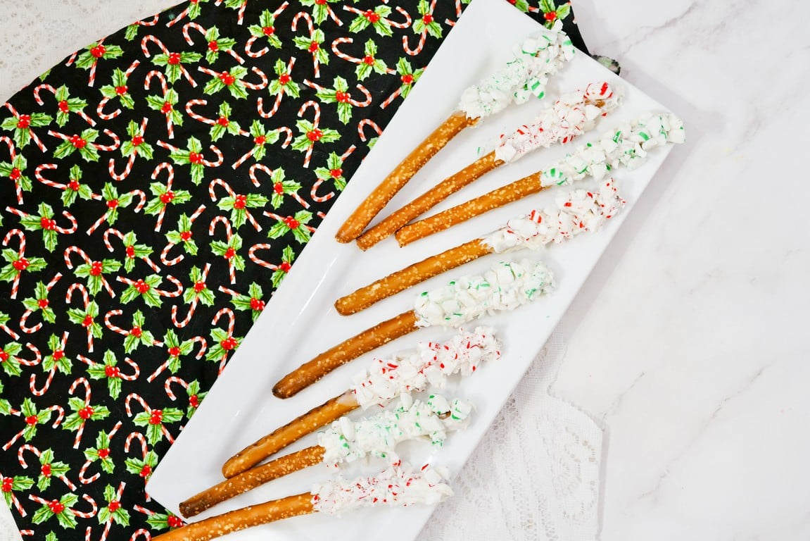 White rectangle plate with pretzels dipped in white chocolate and some with red and white peppermint pieces and some with green and white pieces.