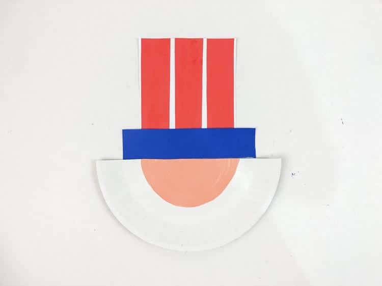 Uncle Sam Paper Plate Craft: three red stripes added to white paper with blue piece added below to form a hat. 