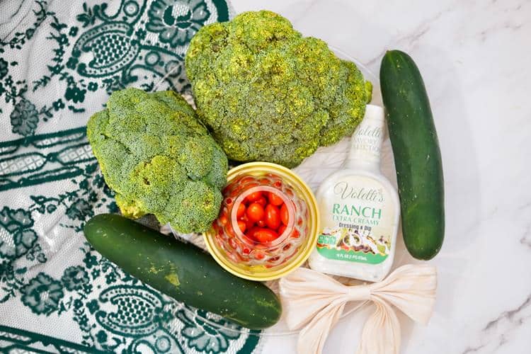 Ingredients required: two large broccoli stalks, container filled with cherry tomatoes, two unsliced cucumbers, a white bow, and a bottle of ranch.