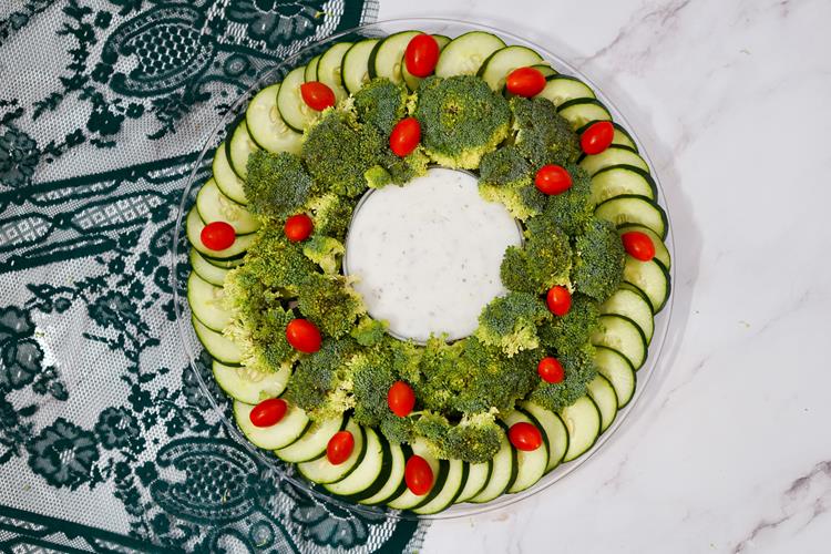 Cherry tomatoes added to broccli and cucumbers to appear as red ornaments on wreath. Large bowl of dip placed in the middle.