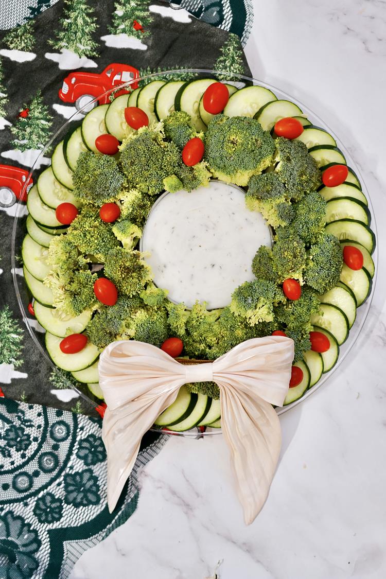 Vegetable Christmas Wreath Platter - Clear round platter with cucumbers on the outside, broccoli inside, big bowl of dip in middle and cherry tomatoes placed randomly on it.