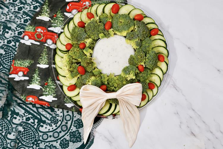 Vegetable Christmas Wreath Platter - cucumbers, broccoli, cherry tomatoes with a large bowl of dip and a bow.