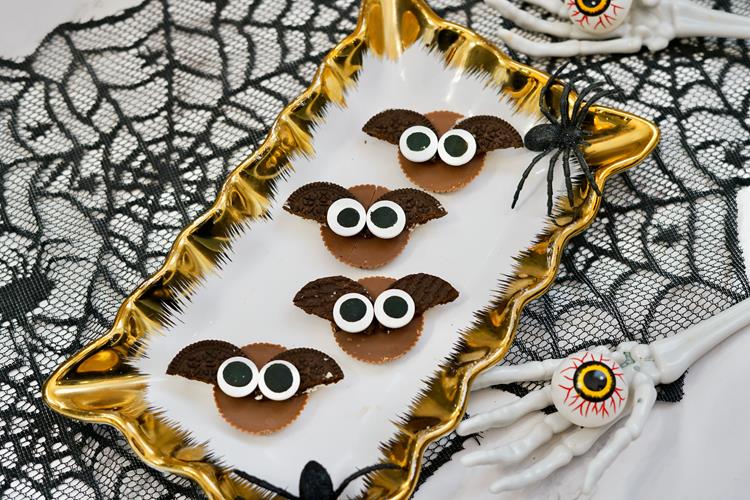 Halloween Reese's Peanut Butter Cup Bats - White and gold plate with four peanut butter cups, Oreos as wings, and candy eyes.