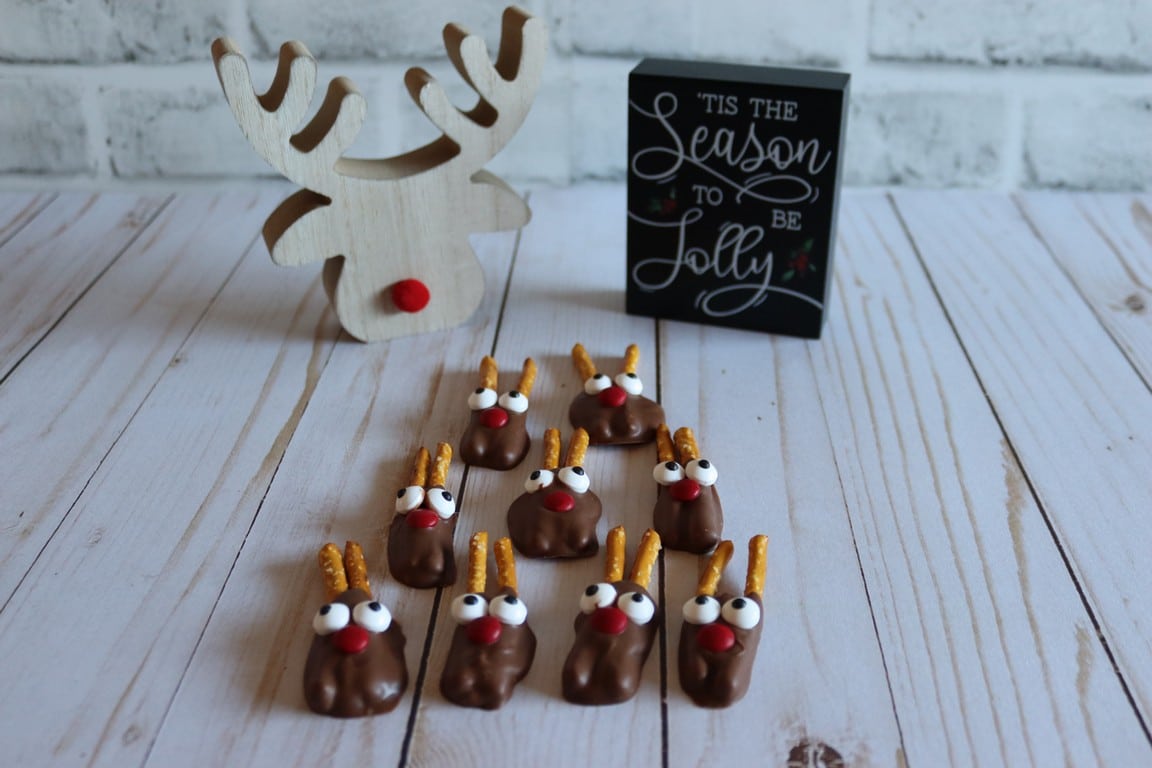 Completed mini pretzel stick reindeers on table with decorate reindeer head in background.