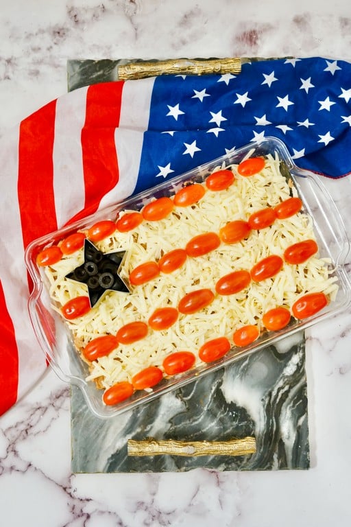 Glass rectangle pan with bean dip, cheese, tomatoes, and olives made to look like a flag. 