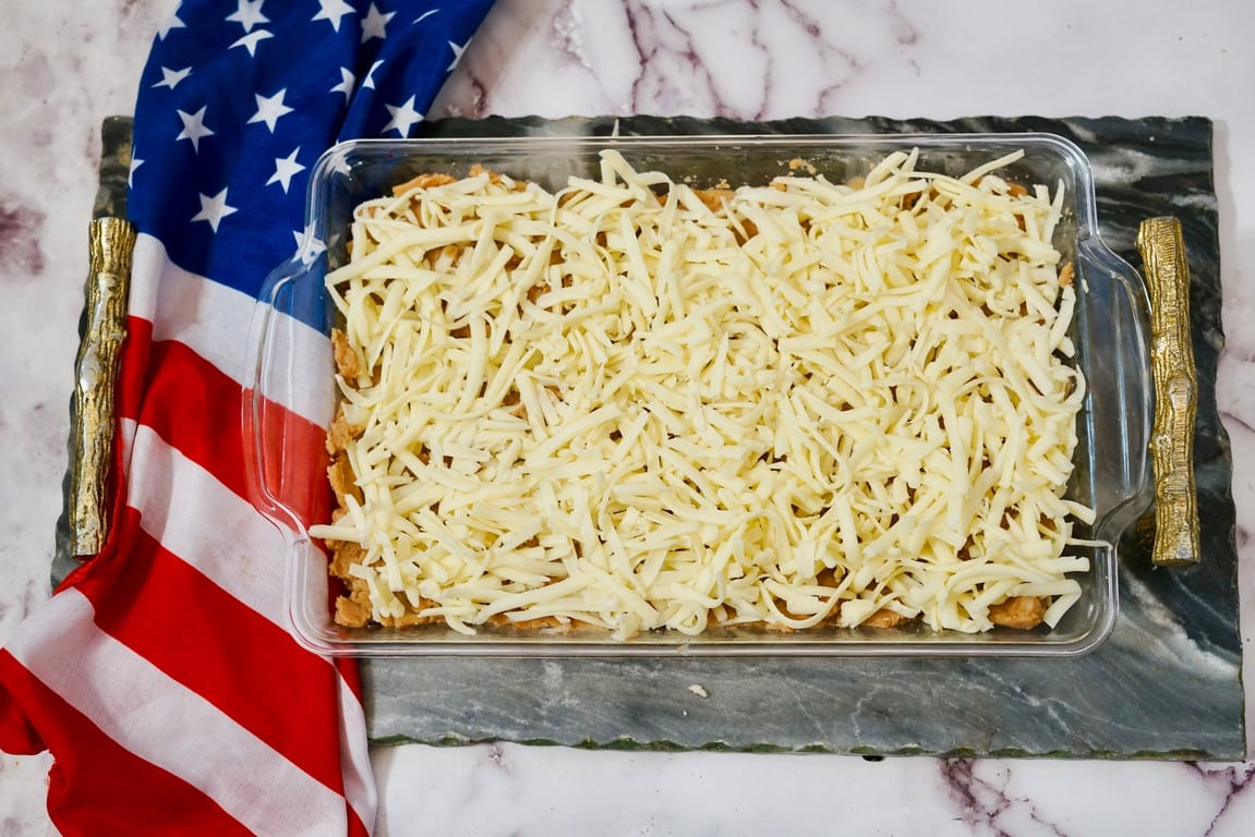 Glass pan with bean layer and cheese added on top. 