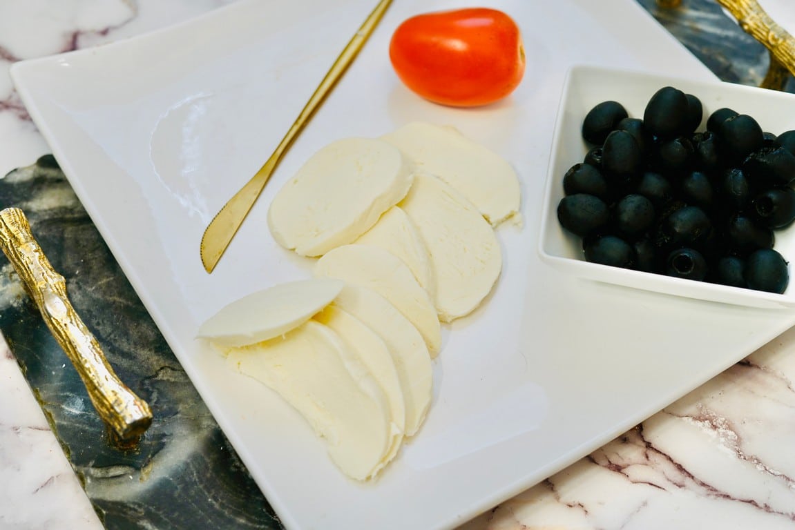White plate with cut up mozzarella and a bowl of black olives. 